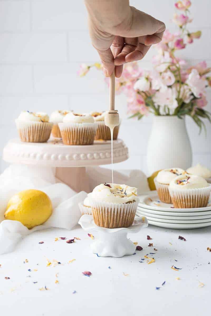 honey lemon cupcake with cream cheese frosting on cupcake stand with honey being drizzled on top